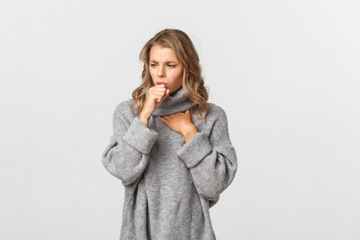 Image of sick woman in grey sweater, coughing and feeling unwell, standing over white background. Concept of health and covid-19.