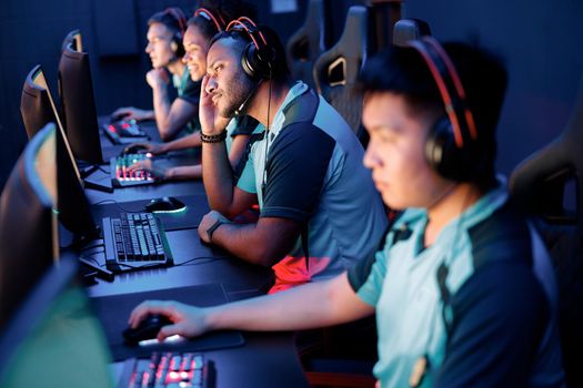 Team of four professional cybersport gamers wearing headphones playing online video games while participating in esports tournament in gaming club
