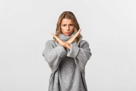 Image of young woman telling no, showing cross to stop something bad, prohibit action and frowning, standing disappointed over white background.