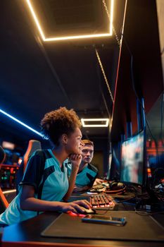 Side view of cute female cybersport gamer playing online game on PC during e-sports tournament in colorful neon lights room