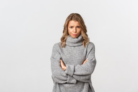 Image of disappointed gloomy girl, frowning and standing defensive, feeling offended or upset, standing over white background.