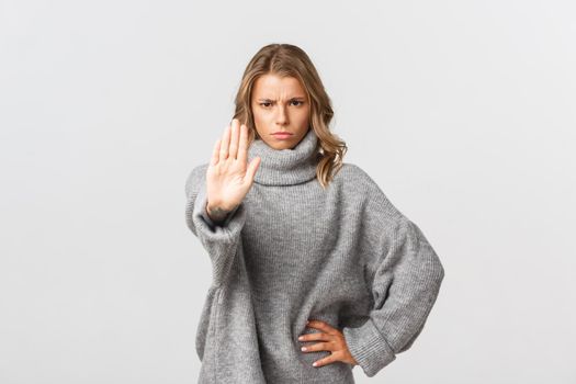 Serious confident woman in grey sweater, extend one arm and telling to stop, prohibit action, frowning disappointed, standing over white background.