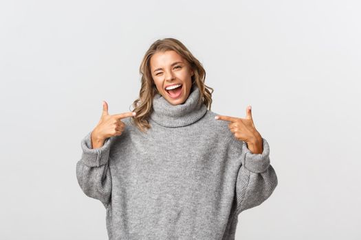 Attractive happy woman in casual clothing pointing at your logo and smiling, winking to encourage you, standing over white background.