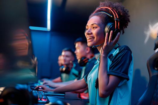 Happy African female gamer wearing headphones looking at PC screen and smile during esports tournament in gaming club