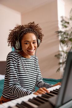 Joyful female musician in headphones looking at camera and smiling while playing melody on electronic musical instrument