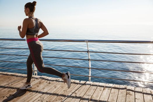 Rear view of female athlete workout on the seaside promenade, jogging near sea.