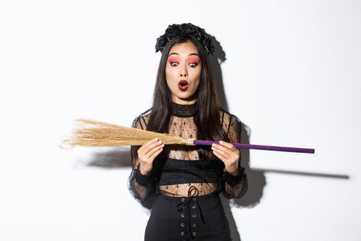 Image of amazed young witch looking at broom with surprised expression. Concept of halloween.