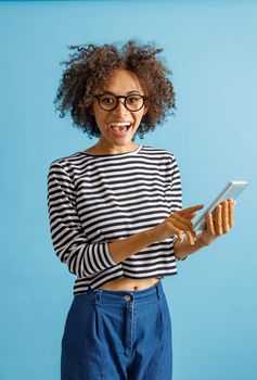 Cheerful multiracial lady looking at camera and laughing while holding modern smartphone. Isolated on blue background