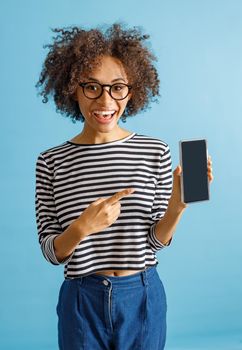 Joyful multiracial lady looking at camera and laughing while holding mobile phone. Isolated on blue background