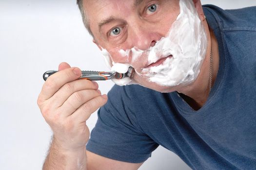 A man's face in shaving foam shaves with a safety razor. Morning or evening exercise, personal hygiene