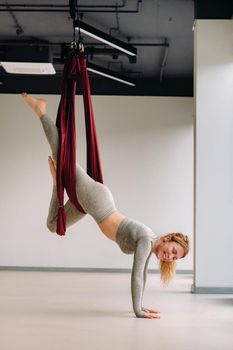 A woman hanging on a hanging hammock does yoga in the gym.