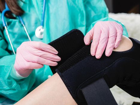 Close-up of the hand of a physiotherapist who helps a patient with a knee brace orthosis after an injury