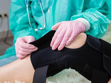 Close-up of the hand of a physiotherapist who helps a patient with a knee brace orthosis after an injury