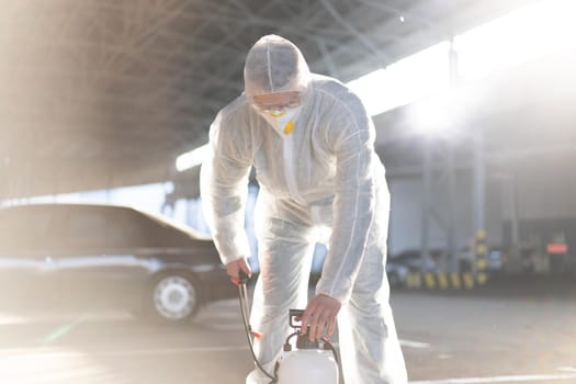 Man dressed white protective overalls spraying surface antibacterial sanitizer sprayer during quarantine Caucasian person protective suit prepares the equipment pumps the pump in the pump