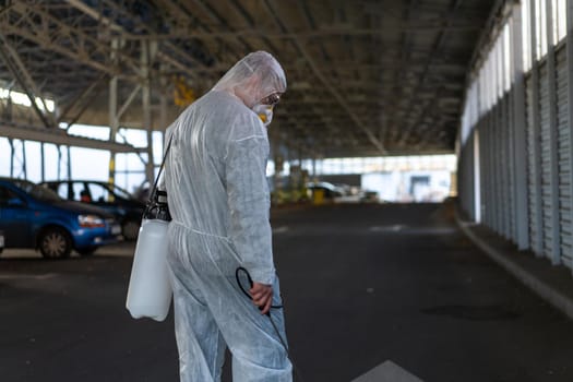 Worker wearing protective suit disinfection gear disinfect surface public place parking. Side view of disinfector safety overall and respiratory mask Covid pandemic disinfection preventive measures