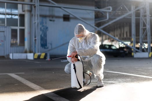 Man dressed white protective overalls spraying surface antibacterial sanitizer sprayer during quarantine Caucasian person protective suit prepares the equipment pumps the pump in the pump