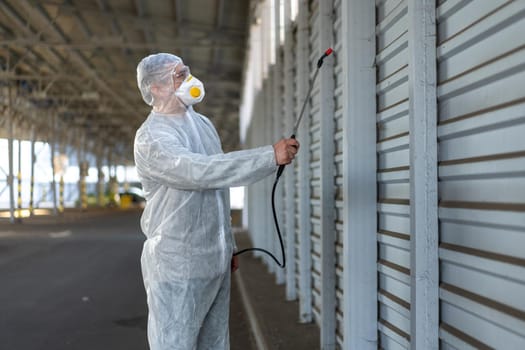 Worker wearing protective suit disinfection gear disinfect surface public place parking. Side view of disinfector safety overall and respiratory mask Covid pandemic disinfection preventive measures