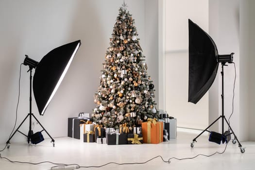 Christmas tree in white interior photo studio with stylish black and orange gift box standing like fashion model with flash light equipment