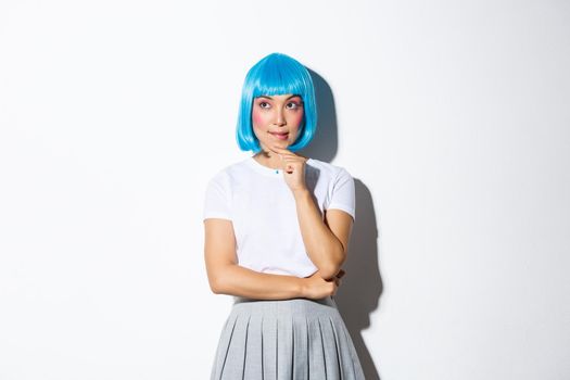 Image of thoughtful kawaii asian girl looking at upper left corner, thinking about something, standing in blue wig, dressed up for party or halloween.