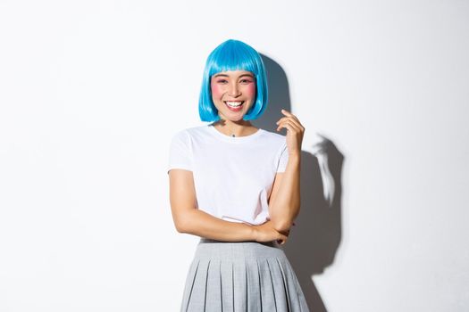 Portrait of happy smiling asian woman in blue shirt wig and shoolgirl costume looking at camera, dressed for halloween party, standing over white background.