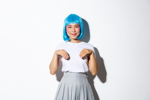 Portrait of cute smiling asian girl in blue wig and schoolgirl costume, playing around and acting like kitten, standing over white background.
