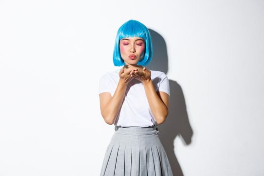 Portrait of beautiful pop girl in blue shirt wig blowing air kiss at camera, close eyes and standing romantic over white background.