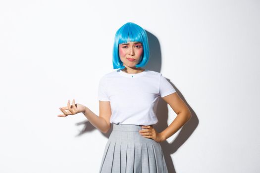 Image of skeptical asian girl in blue wig looking confused and judgemental, standing over white background.