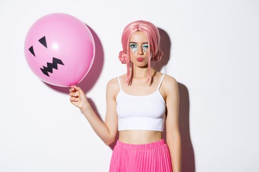 Image of sassy beautiful girl with pink wig and bright makeup, holding balloon at party, winking and looking coquettish, celebrating holiday.