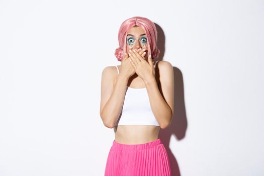 Image of girl smiling and laughing, cover mouth with hands and looking at camera amused, standing in pink wig and bright outfit for halloween party.