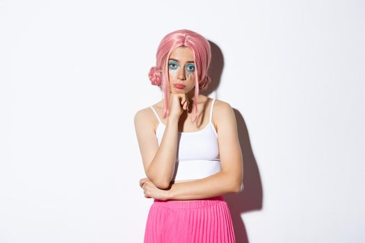 Portrait of sad reluctant girl standing in halloween costume and pink wig, looking bored or disappointed at camera.