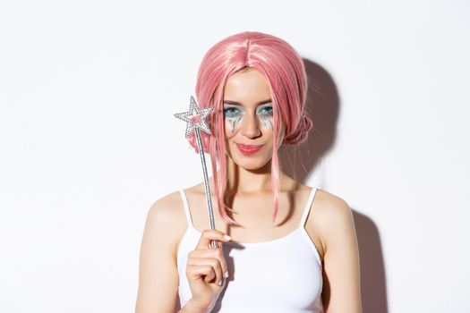 Close-up of sassy attractive woman in halloween outfit for party, holding magic wand and smiling pleased.