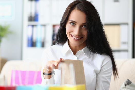Smiling woman unpacking paper shopping bag at home. Buying gifts concept