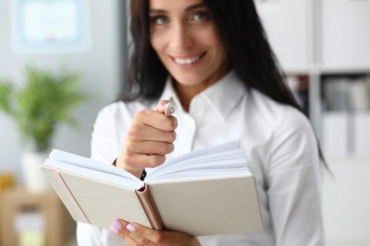 Young businesswoman holding notepad and ballpoint pen in office closeup. Organization and planning concept
