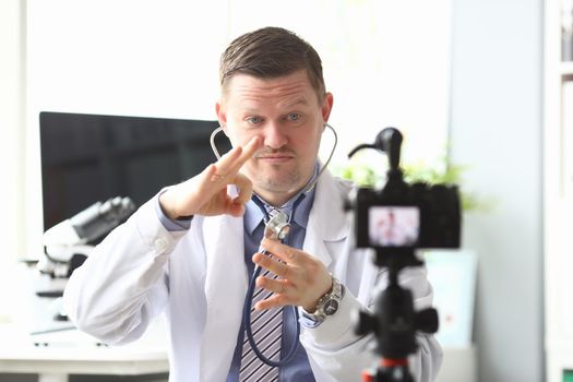 Male doctor banging on stethoscope in front of camera in clinic. Online medical training concept