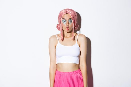 Image of funny female model in pink wig, making silly faces, celebrating halloween in anime character costume, standing over white background.