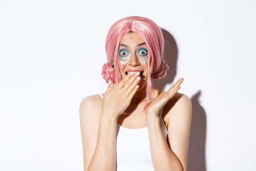 Close-up of surprised glamour girl in pink wig, gasping and smiling amazed, standing over white background.