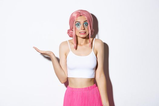 Portrait of clueless cute girl in pink wig shrugging, looking unaware, standing in halloween costume with bright makeup.