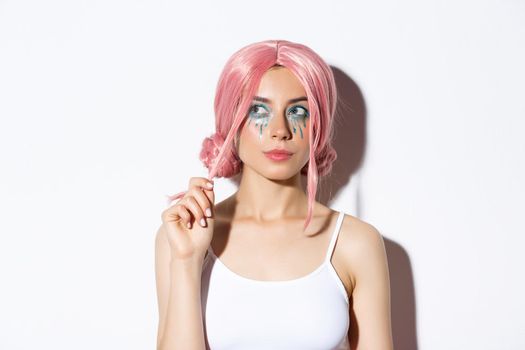 Close-up of thoughtful attractive girl with pink anime wig and bright makeup, looking at upper left corner banner and thinking, making choice, standing over white background.