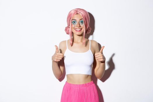 Portrait of satisfied smiling girl showing thumbs-up in approval, praise good choice, standing in halloween costume with pink with and bright makeup.