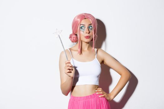 Image of beautiful female with pink wig and bright makeup, holding magic wand, cosplay fairy for halloween party, standing over white background.