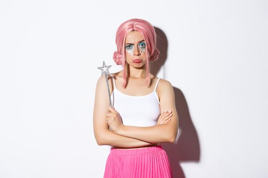 Portrait of moody cute girl in pink wig, dressed as a fairy for halloween, looking upset or disappointed, standing over white background.