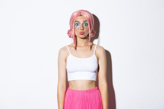 Portrait of beautiful party girl with pink wig and halloween makeup, pouting silly, standing over white background.
