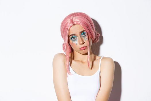 Close-up of silly cute girl in pink wig, looking miserable at camera, wearing halloween costume and makeup.