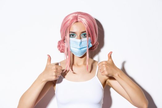 Close-up of beautiful confident girl with pink hair and medical mask, showing thumbs-up, recommend using protective equipment during coronavirus.