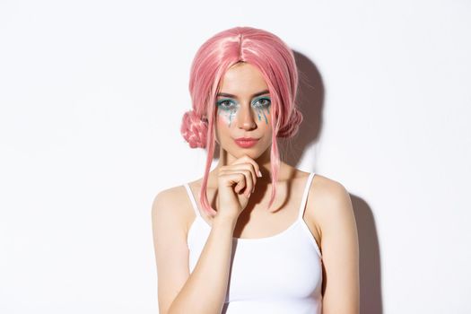 Image of confident woman in pink wig and halloween costume, thinking, looking at camera with interest, standing over white background.