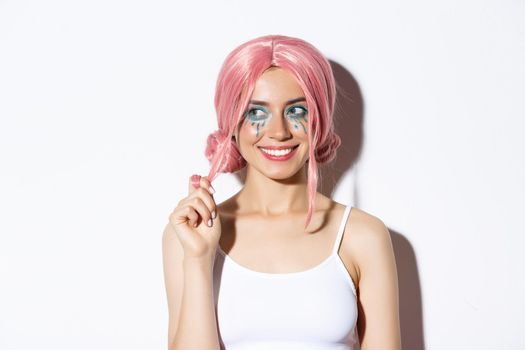 Close-up of coquettish smiling girl in pink wig, looking left intrigued, standing over white background.