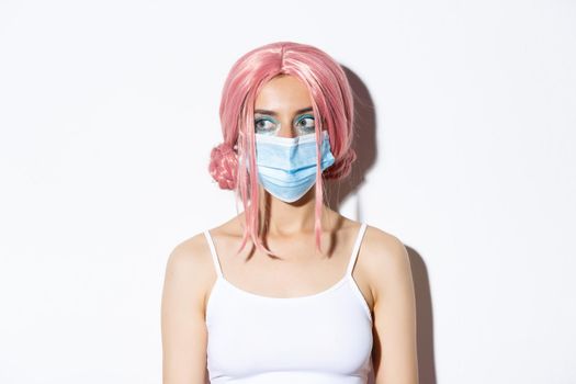 Close-up of young woman in pink wig and medical mask, social distancing during covid-19 pandemic, celebrating halloween with safety measures.