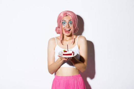 Portrait of cute girl licking lips as holding delicious cake, celebrating birthday, wearing pink wig and bright costume for party.