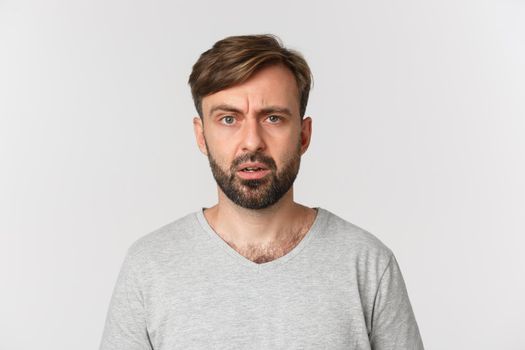 Close-up of handsome confused guy cant understand something, frowning and looking perplexed, standing over white background.