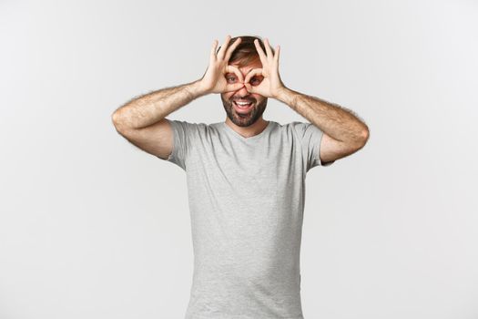 Portrait of funny caucasian guy making faces and mocking someone, standing over white background.